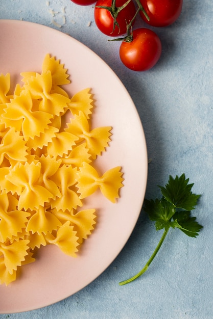 Flat lay uncooked farfalle on plate with tomatoes