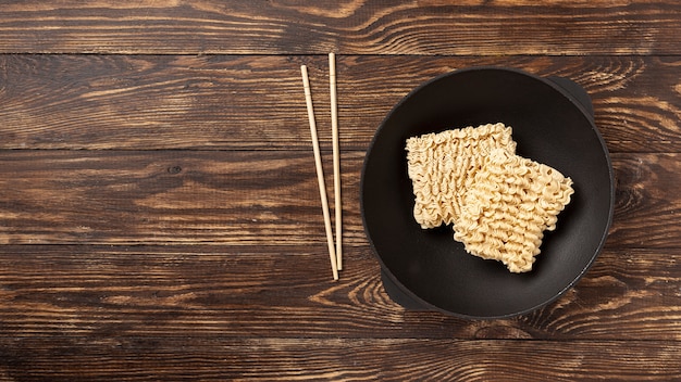 Flat lay uncooked noodles on plate and chopsticks with copy space