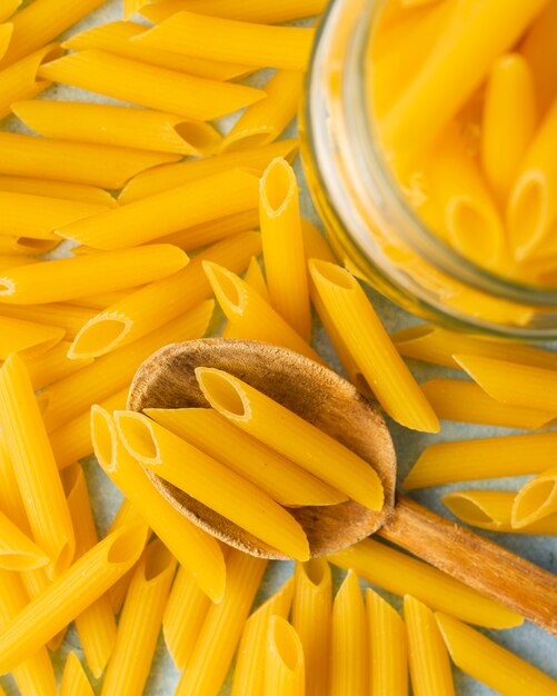 Flat lay uncooked penne with wooden spoon