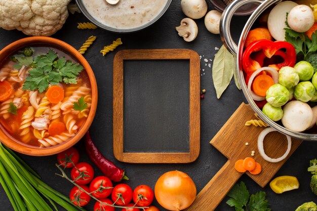 Flat lay vegetables in pan with vegetable soup with fusilli and wooden frame