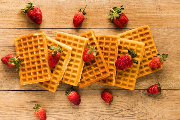 Flat lay of waffles with strawberries on wooden surface