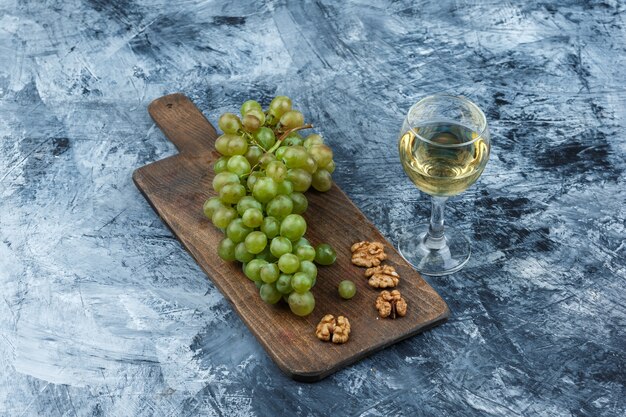 Flat lay white grapes, walnuts on cutting board with glass of wine on dark blue marble background. horizontal