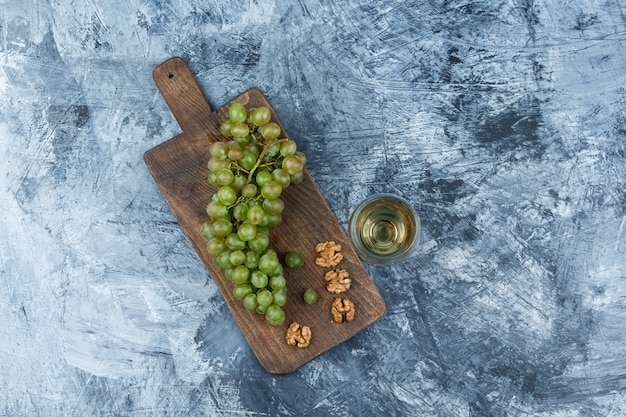 Flat lay white grapes, walnuts in cutting board with glass of wine on dark blue marble background. horizontal