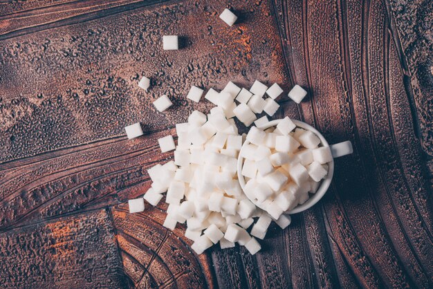 Плоские лежал кубики белого сахара в чашку на темный деревянный стол. горизонтальный