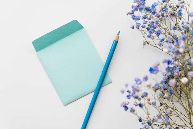 Flat lay with flowers and envelope with pencil 