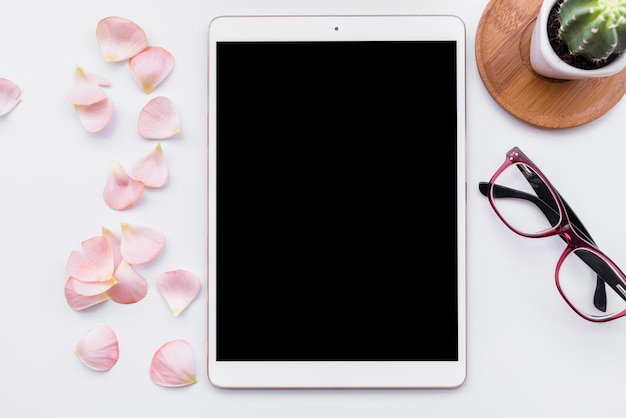 Flat lay with tablet, glasses, cactus and petals on table