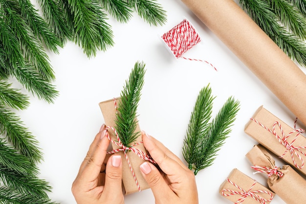 Flat lay of woman hands packing and decorating christmas gifts in frame of christmas tree branches c...