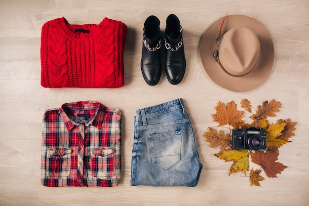 Плоская планировка женского стиля и аксессуаров, красный вязаный свитер, клетчатая рубашка, джинсы из денима, черные кожаные ботинки, шляпа, осенняя модная тенденция, вид сверху, винтажная фотокамера, костюм путешественника