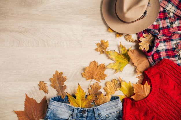 Flat lay of woman style and accessories, red knitted sweater, checkered shirt, denim jeans, hat, autumn fashion trend, view from above, clothes, yellow leaves