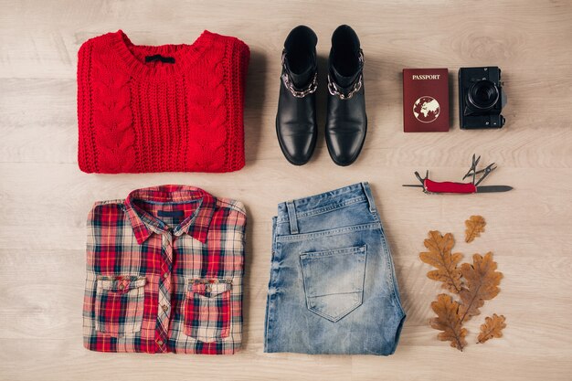 Flat lay of woman style and accessories, red knitted sweater, checkered shirt, jeans, black leather boots, autumn fashion trend, vintage photo camera, swiss knife, passport, traveler outfit