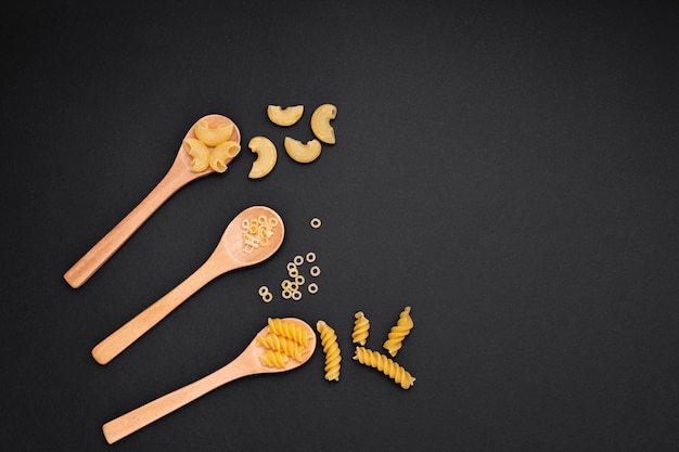 Flat lay wooden spoons with uncooked pasta and copy space