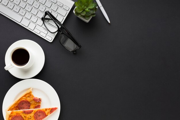 Flat lay of work desk with keyboard and pizza