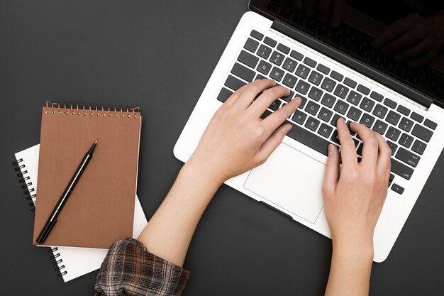 Flat lay of workstation with hands on laptop and notebooks