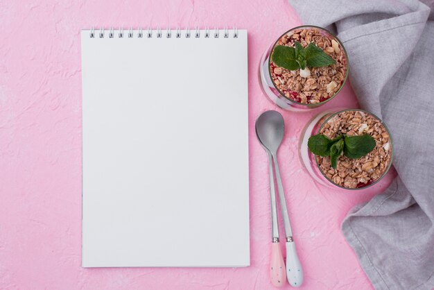 Flat lay of yogurt glasses with cereal and notebook