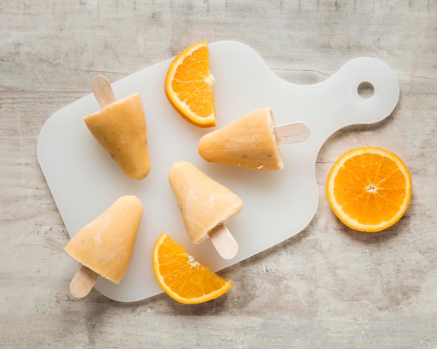 Плоская кладка вкусного фруктового мороженого на разделочной доске с апельсином