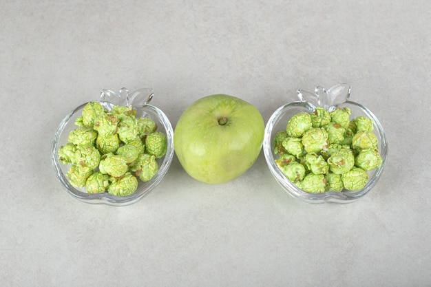 Popcorn aromatizzati riempiti in un porta caramelle a forma di mela con una mela verde nel mezzo su marmo.