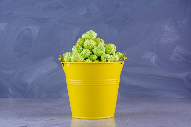 Flavored popcorn piled into a yellow bucket on marble background. High quality photo