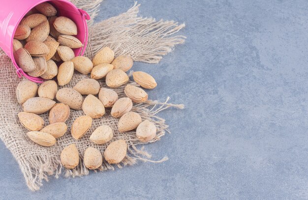 Flavorful almonds spill out of a bowl, on the marble background. 