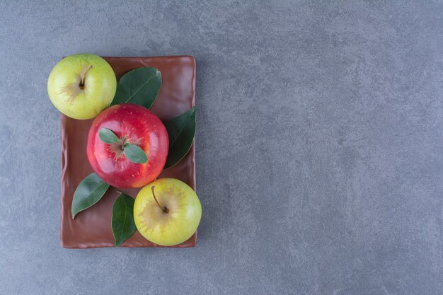 Flavorful apples with leaves on wooden plate on the dark surface