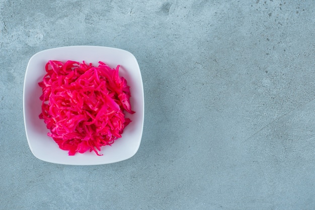 Flavorful chopped red fermented sauerkraut in a bowl , on the blue table. 