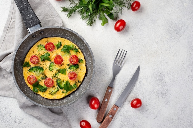 Free photo flay lay of breakfast omelette in pan with tomatoes and cutlery