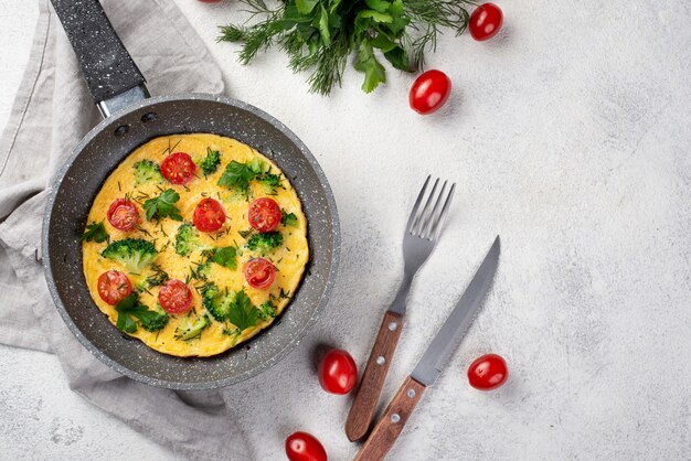 Flay lay of breakfast omelette in pan with tomatoes and cutlery