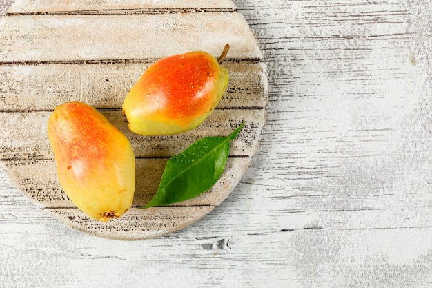 Free photo flesh pears with leaf flat lay on wooden piece and grungy background