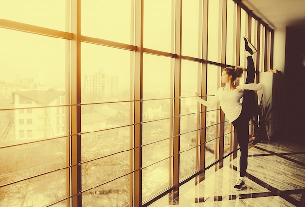 Flexible woman stretching her left leg and looking through the window