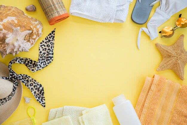 Flip flop near towel with starfish and swimsuit with sunglasses among hat and seashell