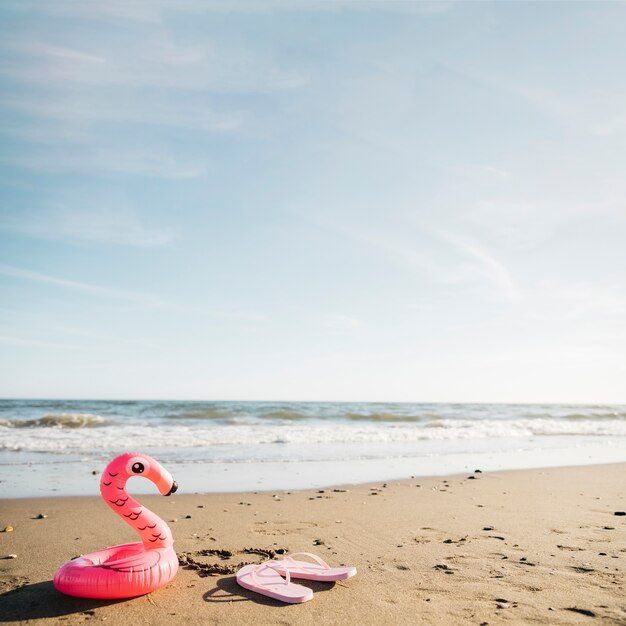 Флип-флоп и надувной фламинго на пляже