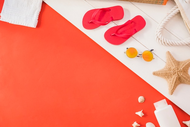 Flip flops near towel with starfish and bottle with sunglasses among seashell 