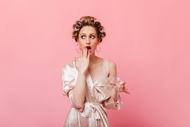 Flirtatious woman in silk robe holding martini glass and covering her mouth in surprise