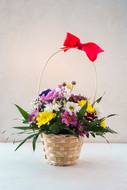 Floral basket with red bow on white table
