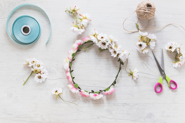 Floral wreath with ribbon; string spool and scissor on white textured background