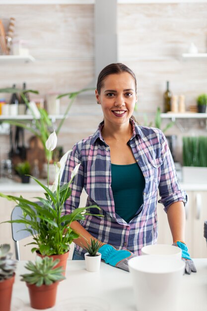 Florist Woman Looking At Camera While Planting Flowers In Kitchen For Home Decoration