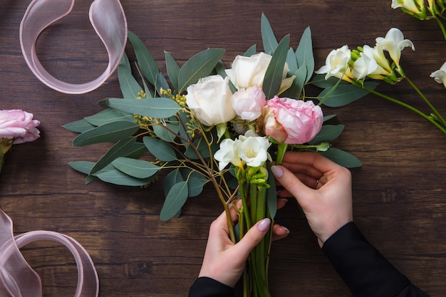 Florist woman making fashion modern bouquet of different flowers on wooden background