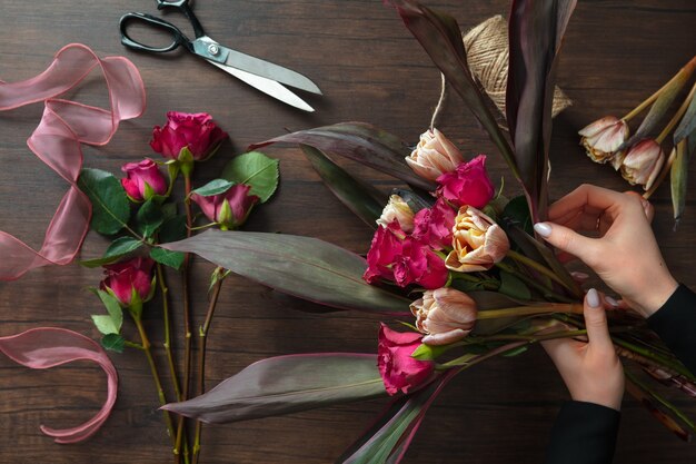 직장에서 플로리스트 : 나무 배경에 다른 꽃의 패션 현대 꽃다발을 만드는 여자. 마스터 반. 결혼식, 어머니, 여성의 날 신부를위한 선물. 로맨틱 한 봄 패션. 열정 장미.