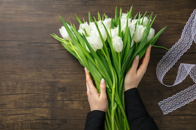 Florist at work: woman making fashion modern bouquet of different flowers on wooden background. Masterclass. Gift for bride on wedding, mother's, woman's day. Romantic spring. Pure white tulips.