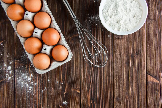 Flour in a bowl with eggs, whisk flat lay on a wooden table