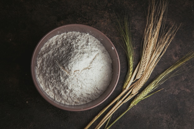 Flour in a bowl with wheat flat lay on a dark brown