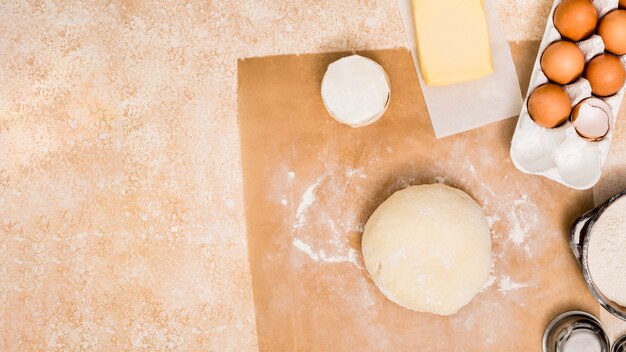 Flour; butter block; eggs and ball of dough on kitchen counter over parchment paper