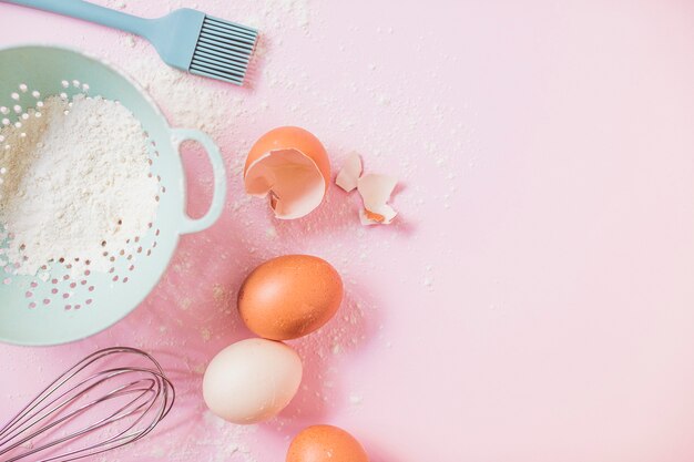 Flour in colander; eggs; whisk against pink background