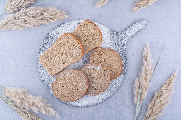 大理石の表面の羽草の茎の横にパンのスライスが付いている小麦粉で覆われたボード