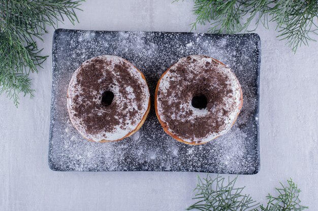 Flour covered platter with two donuts on top on white background.