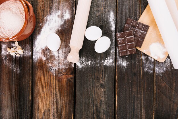 Flour; eggs and chocolate bar with rolling pins and chopping board on table