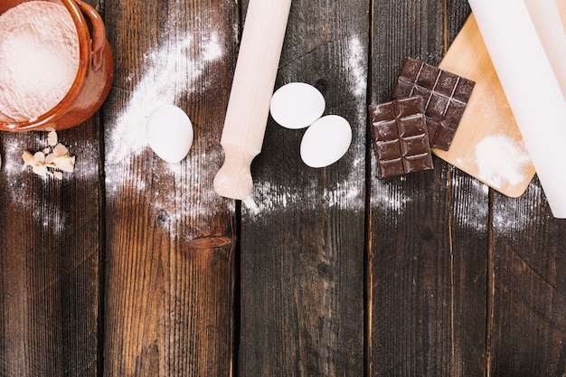 Flour; eggs and chocolate bar with rolling pins and chopping board on table