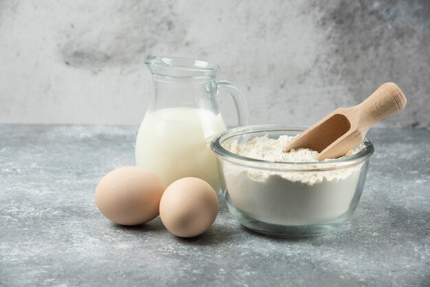 Flour, eggs and jar of milk on marble.