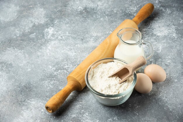 Flour, eggs, milk and rolling pin on marble.