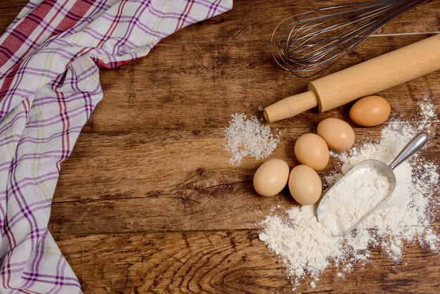 Flour, eggs, salt, towel, rolling pin on wooden table ready for cooking