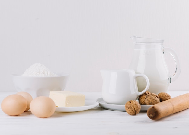 Flour; milk; eggs; cheese; rolling pin and walnuts on white backdrop for making pie